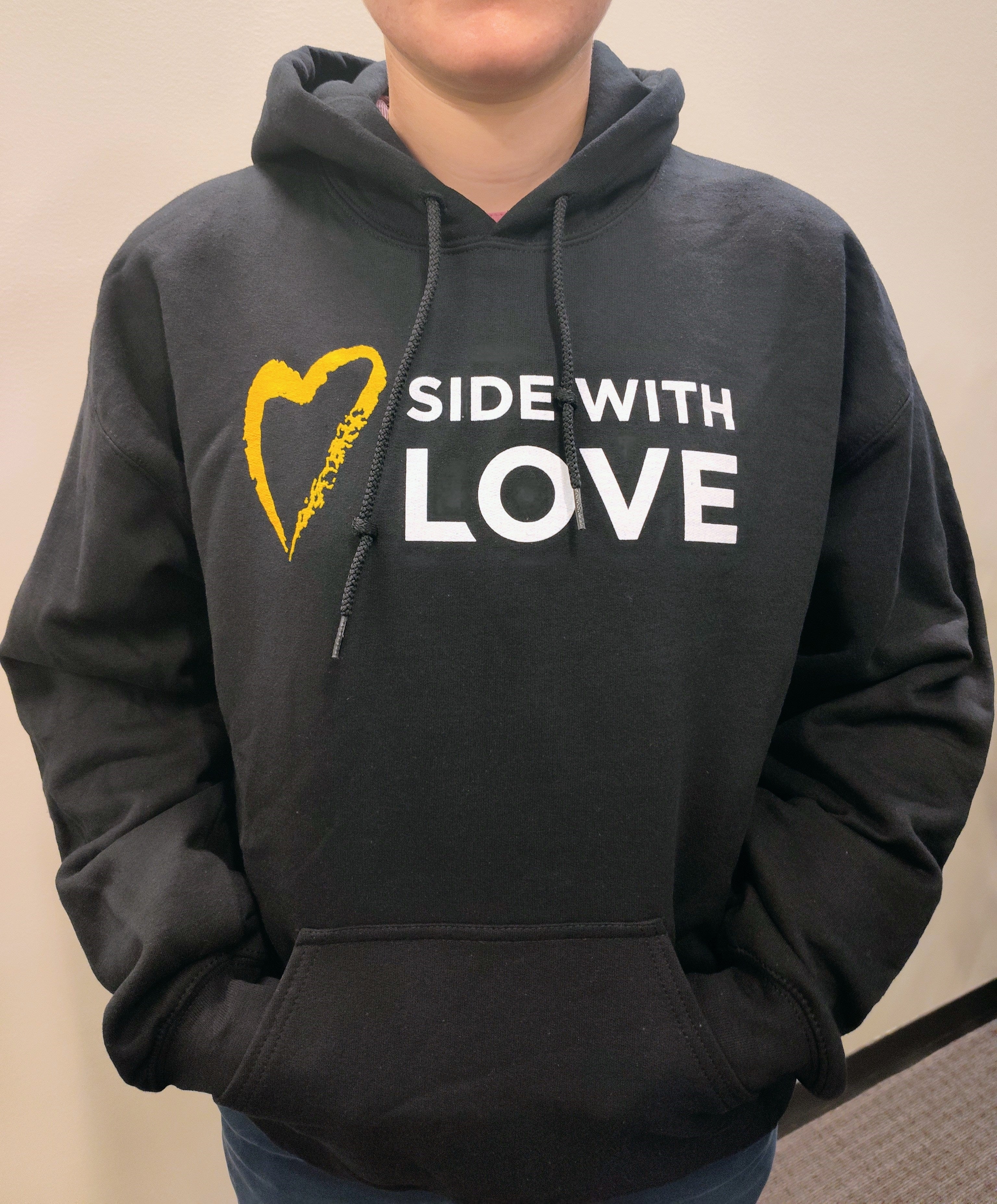 Person wearing a black hoodie with 'SIDE WITH LOVE' and a yellow heart design.